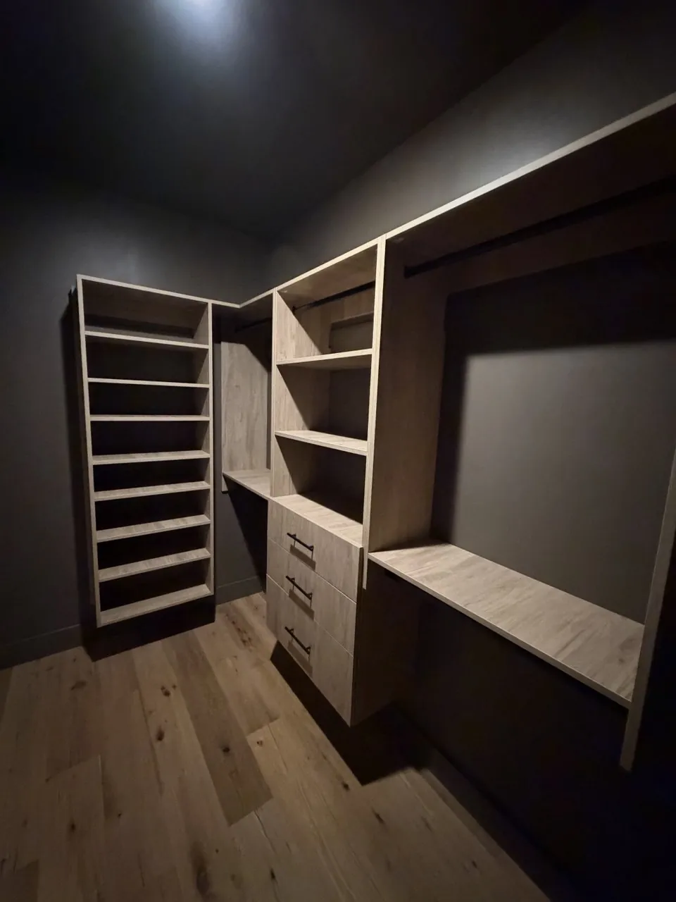Light oak walk-in shelving and drawers set against charcoal walls