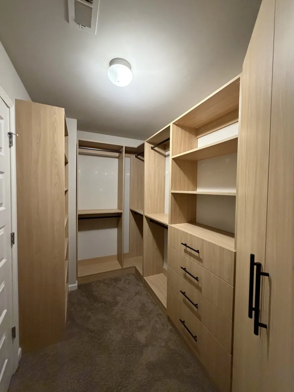 Compact oak walk-in closet with corner shelving and black hardware